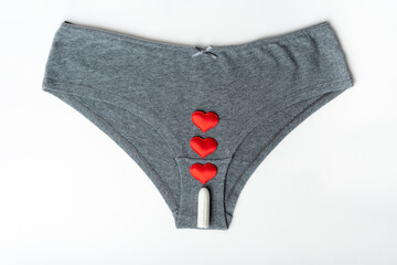 Gray women's panties and a white cotton sanitary tampon and red hearts as mestrual drops on a white background, top view, minimalism. Menstrual cycle. Women's health concept.