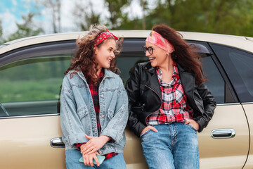 Wall Mural - Automobile's trip. Happy caucasian woman and teen girl standing by a car. The concept of purchase a new automobile and driver's license