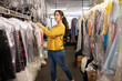 © SuperStock - Side view of mid adult woman looking at camera and putting clothes away on clothing rack