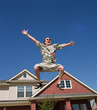 © SuperStock - Middle aged man jumping in front of home, striking a pose mid air