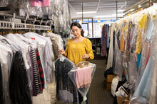 Woman Putting Away Clothing While Working In A Dry Cleaners Shop