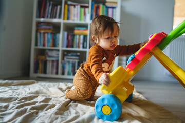 Wall Mural - One small caucasian baby six or seven months old playing with toy on the floor at home in room alone - baby girl having fun examining new toy growing up real people concept copy space