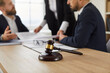 © Studio Romantic - Close up of a judge's gavel on a wooden table, and a group of people working with documents and discussing something in the background. Law and justice, consultation of a lawyer, legal advice concept