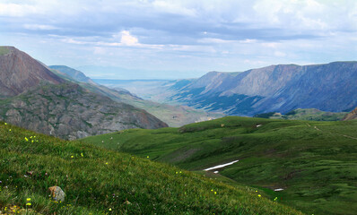 Wall Mural - Panoramic distant view of a wide mountain valley with huge ridges, in the foreground green slopes with a road from the Karagem pass in Altai in summer, a sky with clouds