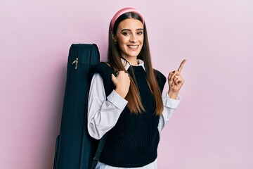 Wall Mural - Beautiful brunette young musician woman wearing guitar case smiling happy pointing with hand and finger to the side