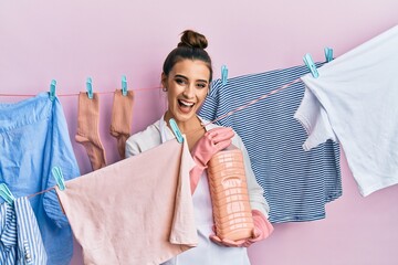 Wall Mural - Beautiful brunette young woman doing laundry holding detergent bottle smiling and laughing hard out loud because funny crazy joke.