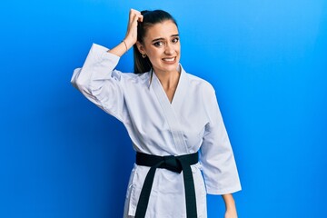 Wall Mural - Beautiful brunette young woman wearing karate fighter uniform with black belt confuse and wonder about question. uncertain with doubt, thinking with hand on head. pensive concept.