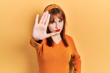 Canvas Print - Redhead young woman wearing casual orange sweater doing stop sing with palm of the hand. warning expression with negative and serious gesture on the face.