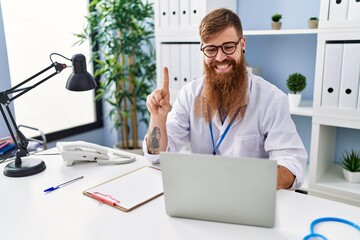 Canvas Print - Redhead man with long beard wearing doctor uniform working using computer laptop smiling with an idea or question pointing finger with happy face, number one