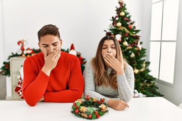 Poster - Young hispanic couple sitting at the table on christmas bored yawning tired covering mouth with hand. restless and sleepiness.