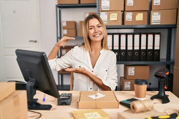 Sticker - Young blonde woman working at small business ecommerce gesturing with hands showing big and large size sign, measure symbol. smiling looking at the camera. measuring concept.