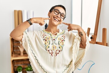 Poster - Young hispanic woman with short hair at art studio smiling cheerful showing and pointing with fingers teeth and mouth. dental health concept.