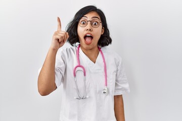 Wall Mural - Young hispanic doctor woman wearing stethoscope over isolated background pointing finger up with successful idea. exited and happy. number one.