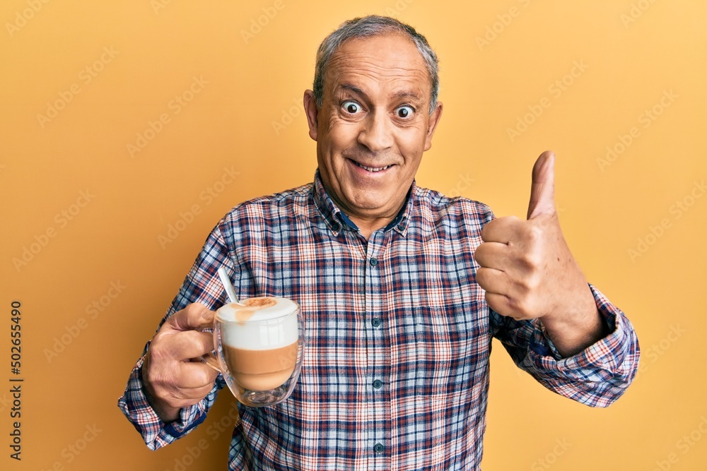 Handsome senior man with grey hair drinking a cup coffee approving doing positive gesture with hand, thumbs up smiling and happy for success. winner gesture.