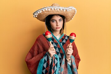 Canvas Print - Young caucasian woman holding mexican hat using maracas relaxed with serious expression on face. simple and natural looking at the camera.