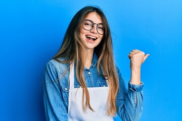 Wall Mural - Young caucasian woman wearing apron smiling with happy face looking and pointing to the side with thumb up.