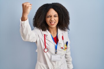 Wall Mural - Young african american woman wearing doctor uniform and stethoscope angry and mad raising fist frustrated and furious while shouting with anger. rage and aggressive concept.