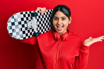 Poster - Young latin woman holding skate celebrating achievement with happy smile and winner expression with raised hand