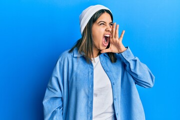 Poster - Young latin woman wearing cute wool cap shouting and screaming loud to side with hand on mouth. communication concept.