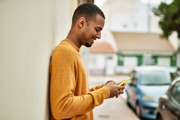 Wall Mural - Young african american man smiling happy using smartphone at the city.