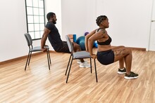 Young African American Couple Training Using Chair At Sport Center.
