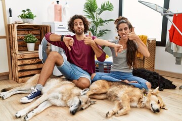 Wall Mural - Young hispanic couple doing laundry with dogs doing thumbs up and down, disagreement and agreement expression. crazy conflict