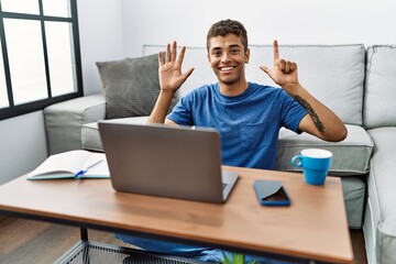 Sticker - Young handsome hispanic man using laptop sitting on the floor showing and pointing up with fingers number seven while smiling confident and happy.