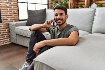 Wall Mural - Young hispanic man smiling confident talking on the smartphone at home