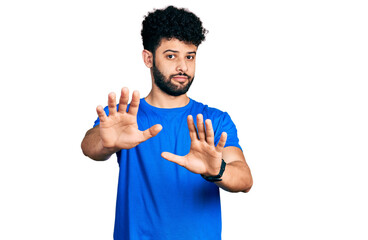 Young arab man with beard wearing casual blue t shirt moving away hands palms showing refusal and denial with afraid and disgusting expression. stop and forbidden.