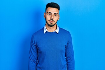 Wall Mural - Young hispanic man with beard wearing casual blue sweater relaxed with serious expression on face. simple and natural looking at the camera.