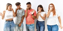 Group Of Young Friends Standing Together Over Isolated Background Smelling Something Stinky And Disgusting, Intolerable Smell, Holding Breath With Fingers On Nose. Bad Smell