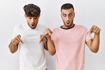 Canvas Print - Young gay couple standing over isolated background pointing down with fingers showing advertisement, surprised face and open mouth