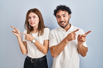 Sticker - Young couple wearing casual clothes standing together pointing aside worried and nervous with both hands, concerned and surprised expression