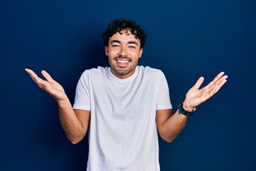 Poster - Young hispanic man wearing casual white t shirt celebrating victory with happy smile and winner expression with raised hands