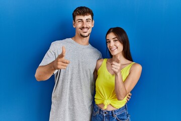 Poster - Young hispanic couple standing together over blue background pointing fingers to camera with happy and funny face. good energy and vibes.