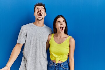 Poster - Young hispanic couple standing together over blue background angry and mad screaming frustrated and furious, shouting with anger. rage and aggressive concept.