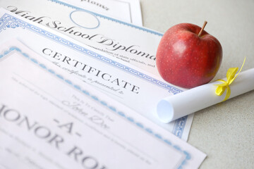 Wall Mural - A honor roll recognition, certificate of achievement and high school diploma lies on table with small scroll and red apple. Education documents