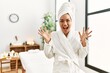 © Krakenimages.com - Young brunette woman wearing towel and bathrobe standing at beauty center celebrating crazy and amazed for success with arms raised and open eyes screaming excited. winner concept