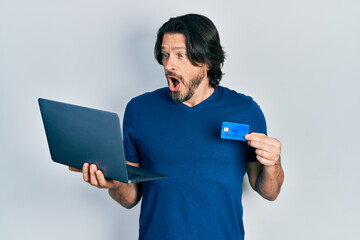 Canvas Print - Middle age caucasian man wearing business style holding laptop and credit card celebrating crazy and amazed for success with open eyes screaming excited.