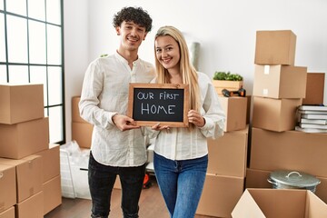 Poster - Young beautiful couple smiling happy holding blackboard with our first home message.