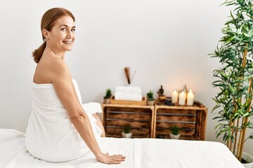 Poster - Middle age caucasian woman wearing towel sitting on massage board at beauty center