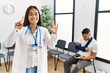 © Krakenimages.com - Young asian doctor woman at waiting room with a man with a broken arm showing and pointing up with fingers number six while smiling confident and happy.