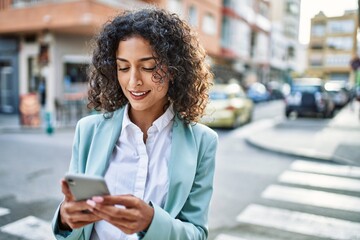 young hispanic business woman wearing professional look smiling confident at the city using smartpho
