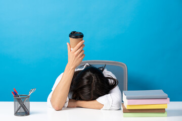 Wall Mural - Woman sleeping head on desk showing disposable cup of coffee isolated on blue background. Caffeine addiction concept