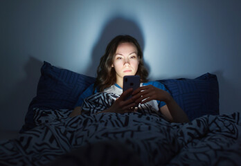 The girl lies at home in the evening on the bed with a phone in the dark. defocus