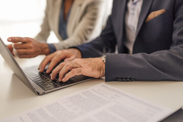 Senior businessman using laptop while sitting with colleague at office desk