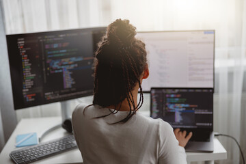 Wall Mural - rear of female web expert typing on computer looking at monitors while sitting indoors