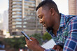© Meeko Media - A Black businessman texts on cellphone during his coffee break on office balcony