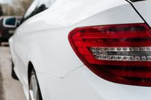 Rear Red Headlight Of White Modern Car Sedan Parked On Street. Close-up, Back View