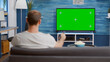 © DC Studio - Man looking at green screen on tv and switching channels sitting on couch in modern living room with bowl of popcorn. Person relaxing on sofa using television remote zapping programs on chroma key